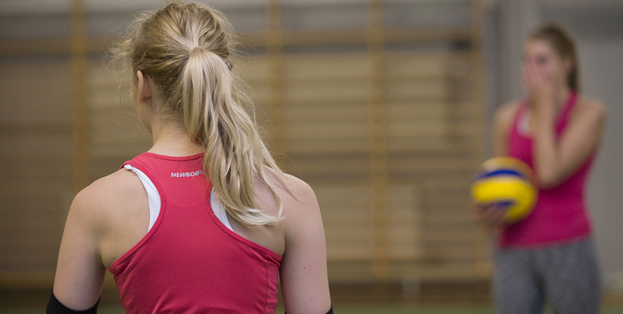 Tjej i sporthallen, i bakgrunden en tjej med volleyboll.