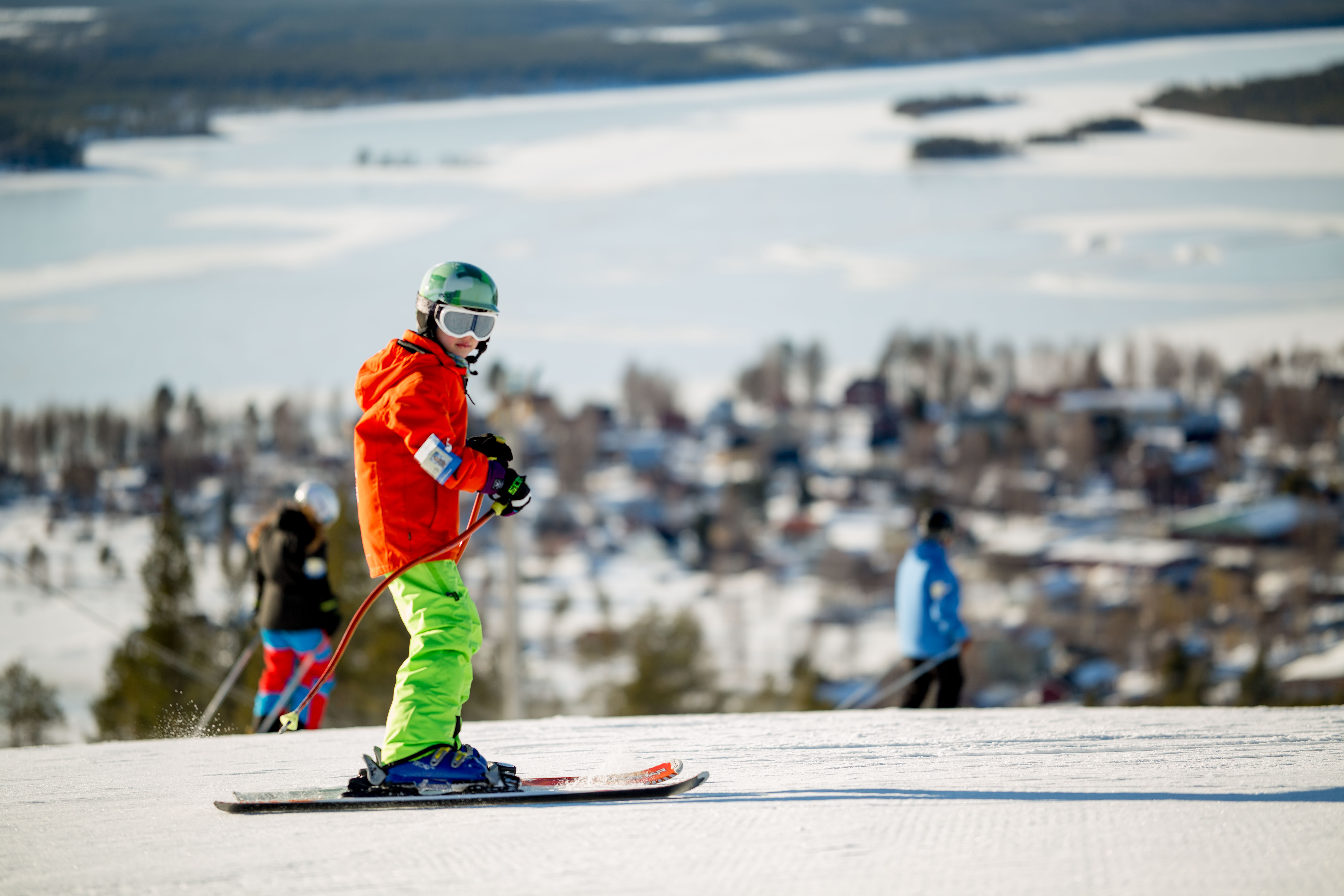 Pojke med orange täckjacka, gröna täckbyxor och hjälm med glasögon som åker slalom i Tjamstanbackarna.