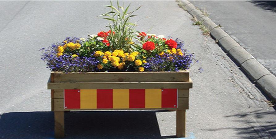 En blomlåda med blommor i och reflexer utanpå står på gatan 